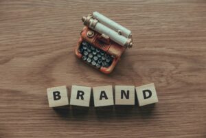 Top view of typewriter and wooden cube with text BRAND on wooden background.